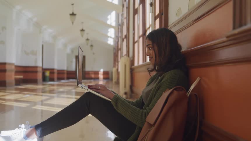 A student at a college sits on the floor and types on her laptop