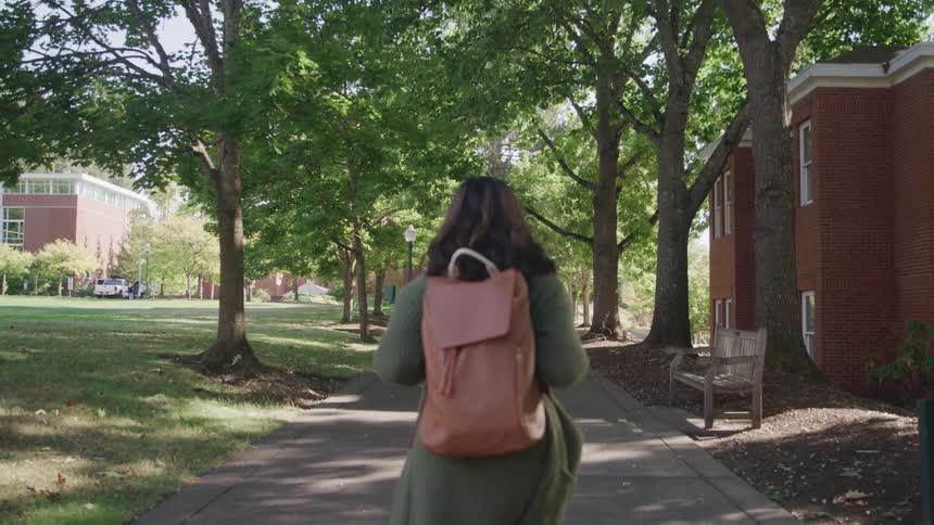 Female student walking through the campus of a university with a backpack on her back