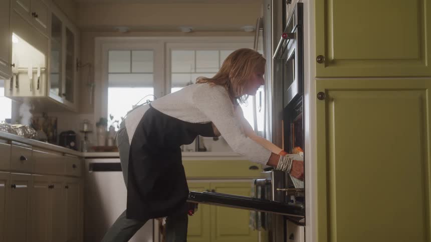 Woman taking out large cooked turkey from oven and setting it on counter
