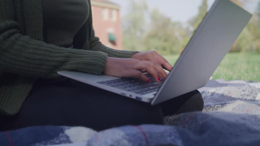 A woman is typing on her laptop while sitting on the grass