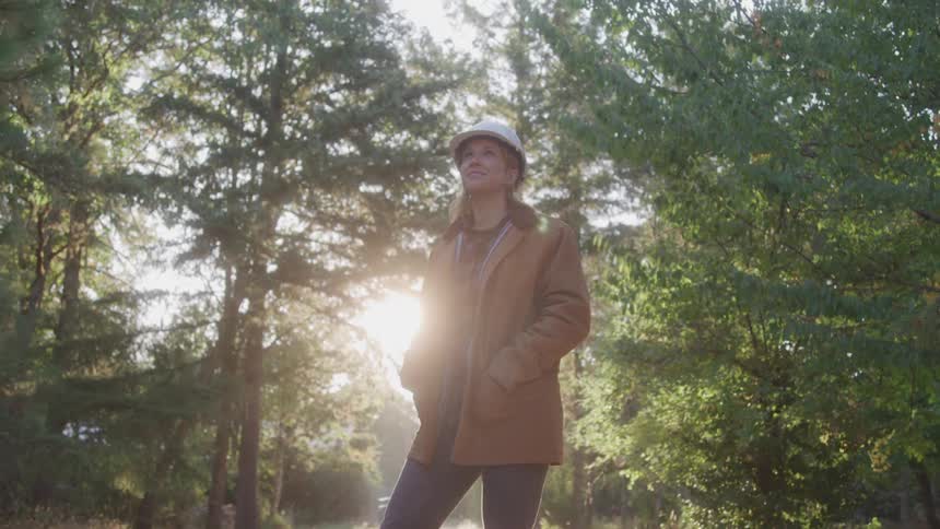 Woman in a coat and a white helmet in the middle of a forest