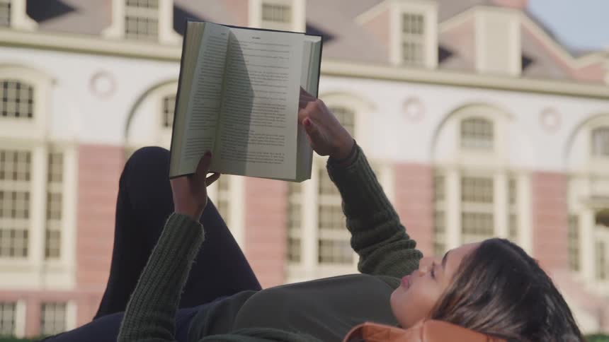 Woman lying outdoors and reading a book