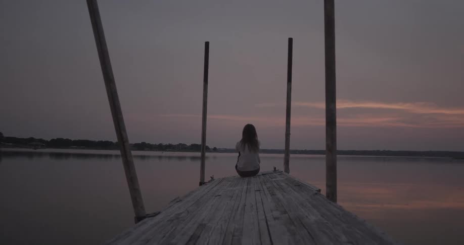 A person sits on a dock at sunset