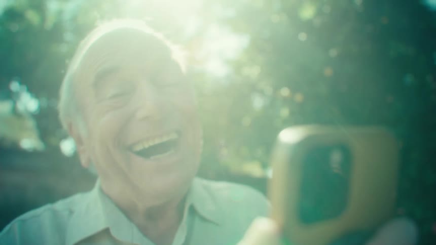 Happy elderly man chatting in the backyard with a smartphone