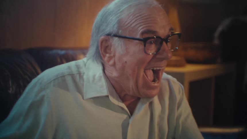 Man laughs cheers and pumps his arms in reaction to what is he is watching on his smart phone