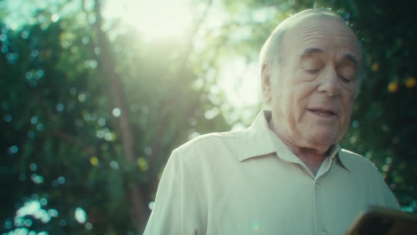 Elderly man wearing a white collared shirt interacting with a smartphone in outdoor