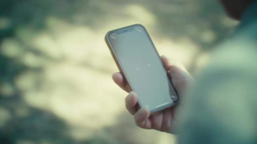 The video shows a closeup of a persons hand holding a smartphone with a blank dark screen the phone case appears to be a light brown or tan color