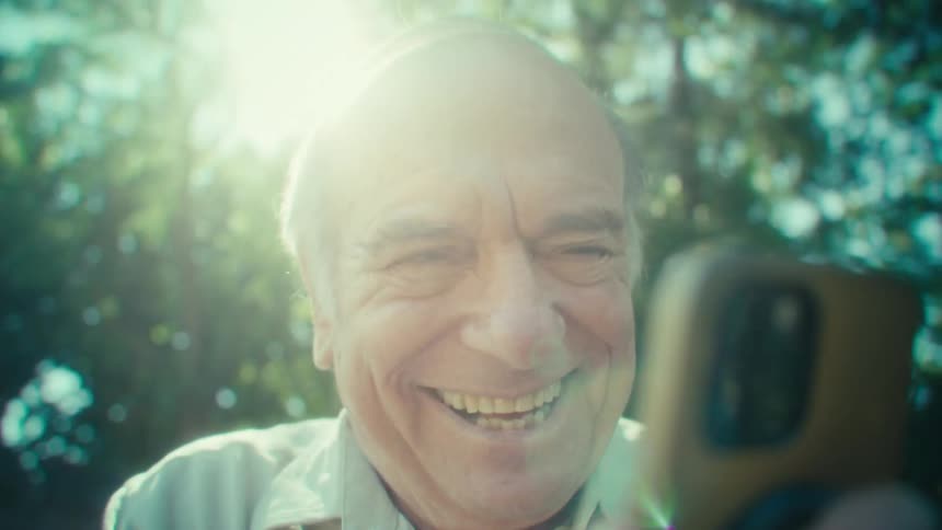 The man laughs and talks to his cell phone while moving in his yard
