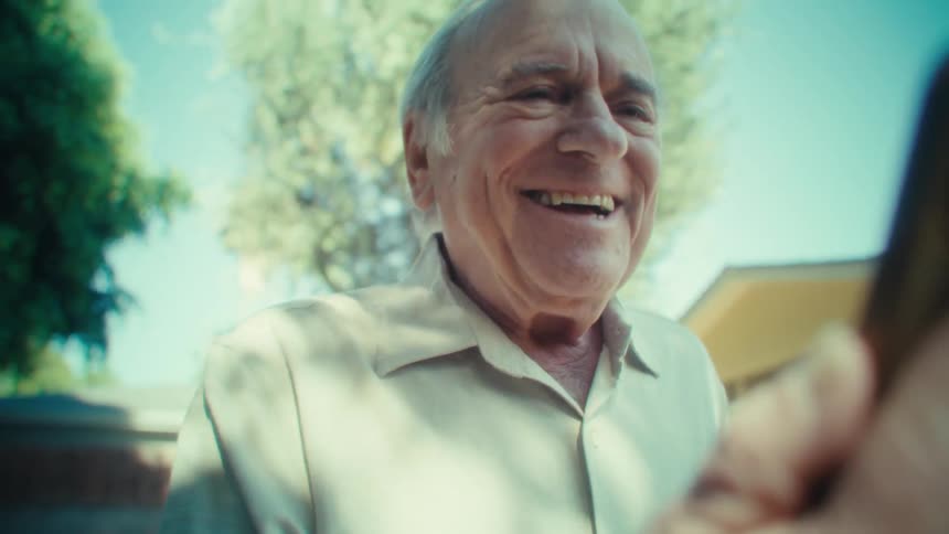 Elderly man happily interacting with a smartphone while walking through a backyard