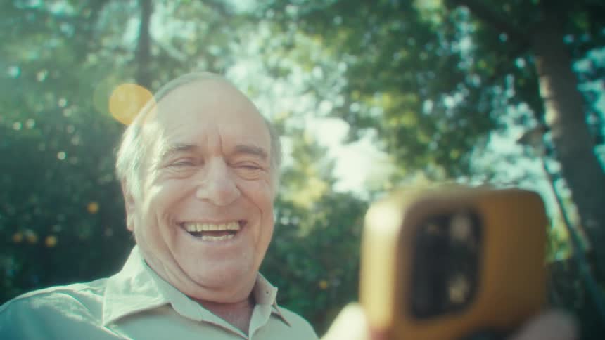 Elderly man in a backyard interacting with a smartphone with a happy expression