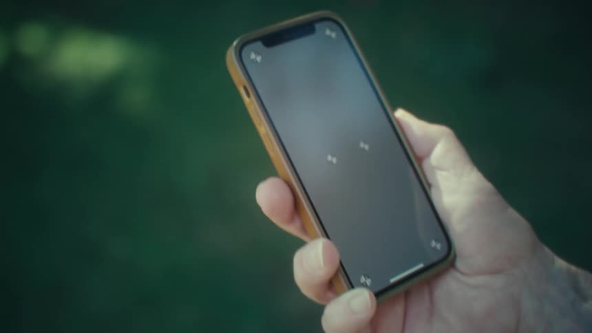 Elderly man views a smartphone while walking outdoors during the daytime