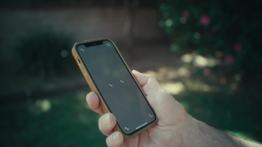 Men holding a cellphone in outdoor environment with grass and plants on the back