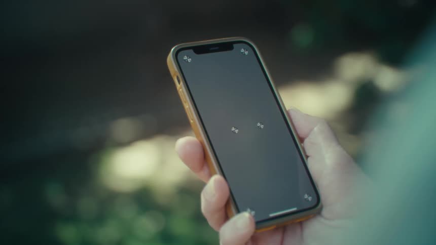 The video shows a closeup of a person holding a smartphone with a blank dark screen and a light brown or tan case