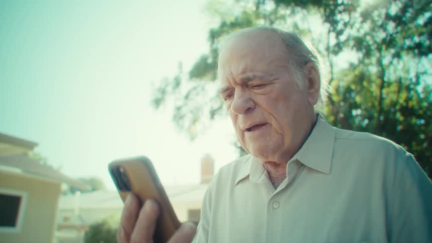 Elderly man walking through a yard and talking on a smartphone