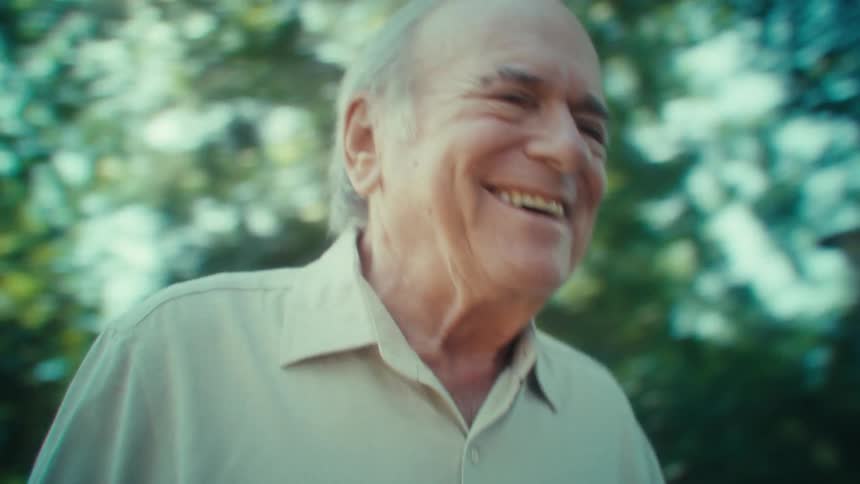Elderly man making a video call while walking outdoors on a sunny day laughs