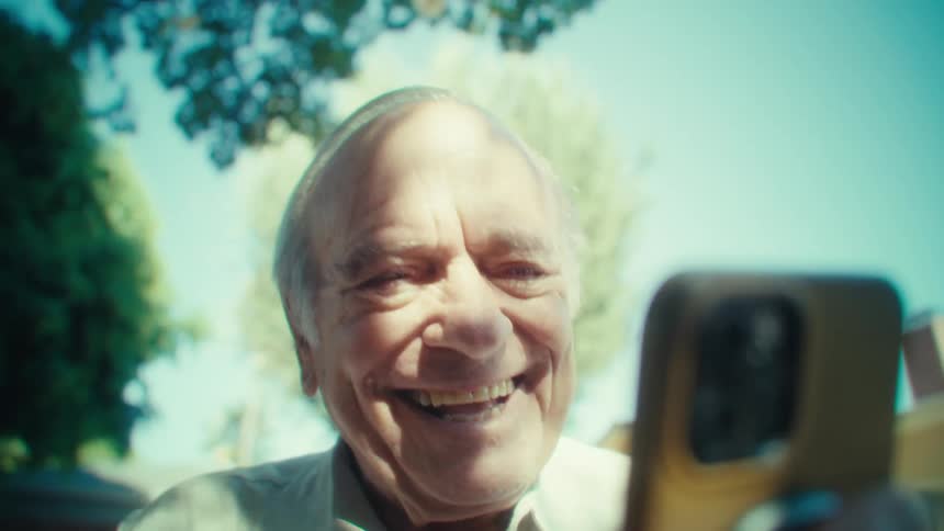 Elderly man happy laughing to a smartphone with trees in the back