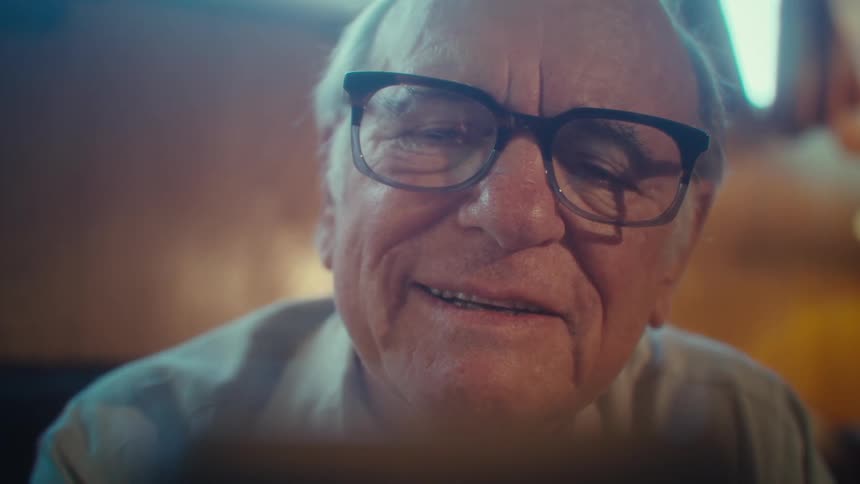 Elderly man smiles warmly while looking at smartphone indoors