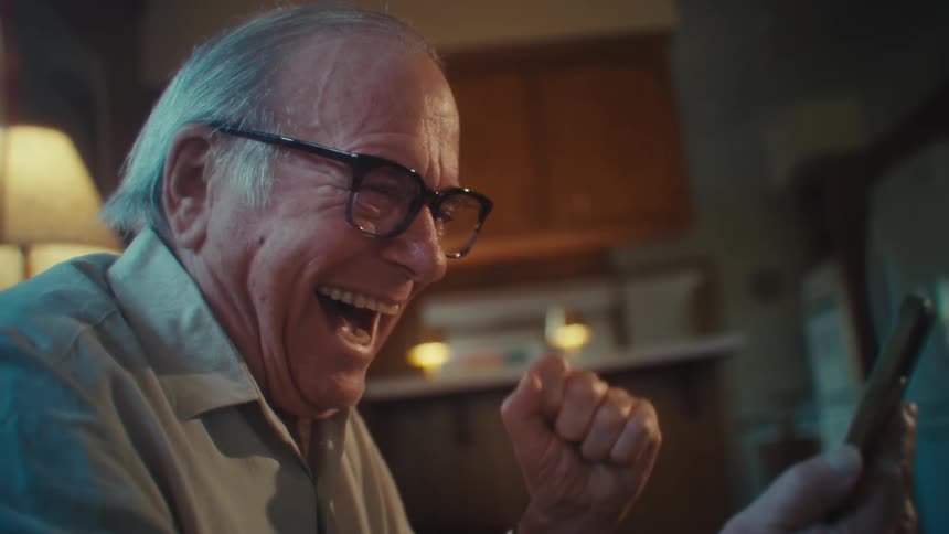Elderly man interacting with a smartphone and jumping for joy