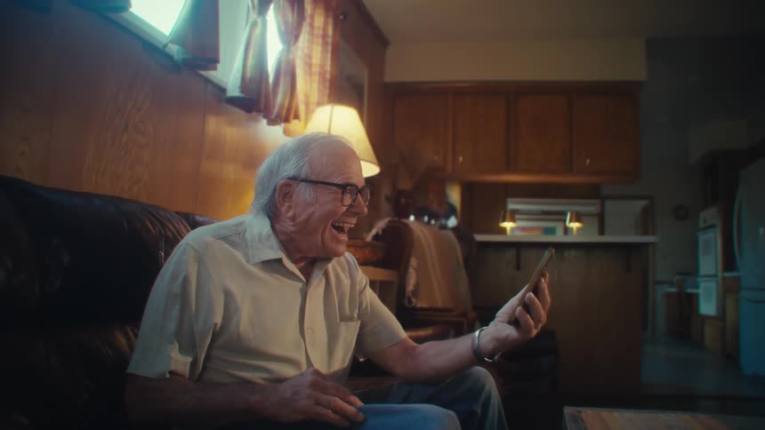 Elderly man sitting on a couch happy and laughing to his smartphone