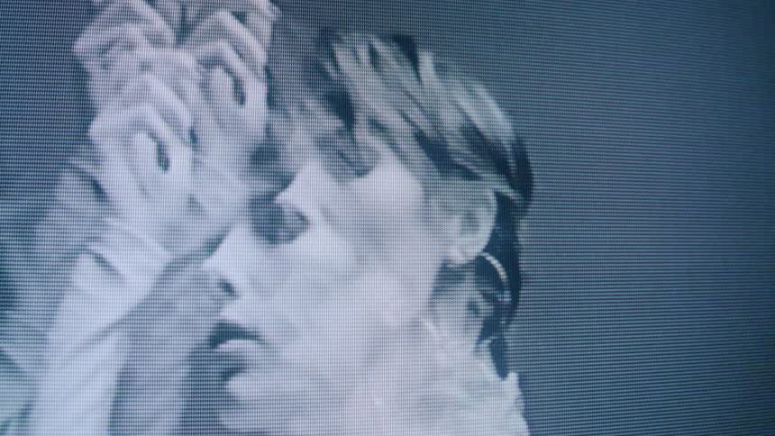 The video displays an abstract monochromatic black and white closeup of a persons face with a pixelated or grainy effect giving it a somewhat digital or vintage television appearance the face is predominantly shown in profile but occasionally turn