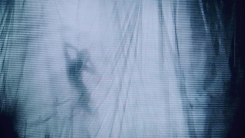 The video displays an abstract visual of a humanlike silhouette possibly made of light or an ethereal substance surrounded by rapidly moving streaking vertical lines that give the impression of falling rain or light the overall effect is monochromati