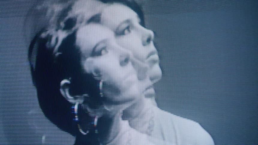 A distorted monochrome closeup of a person with short hair and hoop earrings appears on a pixelated screen creating a ghostly doubleexposure effect