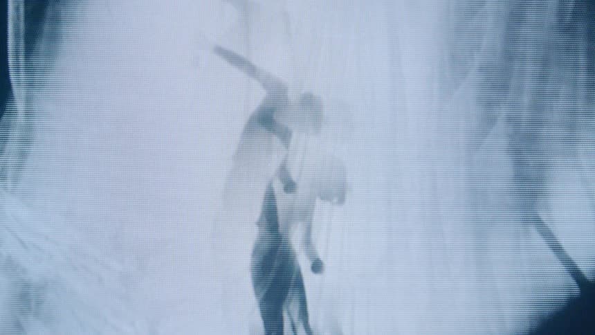 The video displays an abstract monochromatic blue and white visual of a persons silhouette with a grainy or pixelated effect appearing to dance or move rhythmically against a misty or smoky backdrop the figure is semitransparent and in constant mo