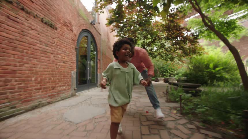 A father running and having fun with his son on the sidewalk at midday surrounded by trees