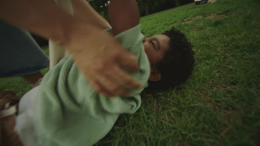 A child lies laughing on the grass while being playfully tickled by a person