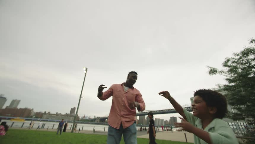 A black man and his son are playing with a toy rocket in a park