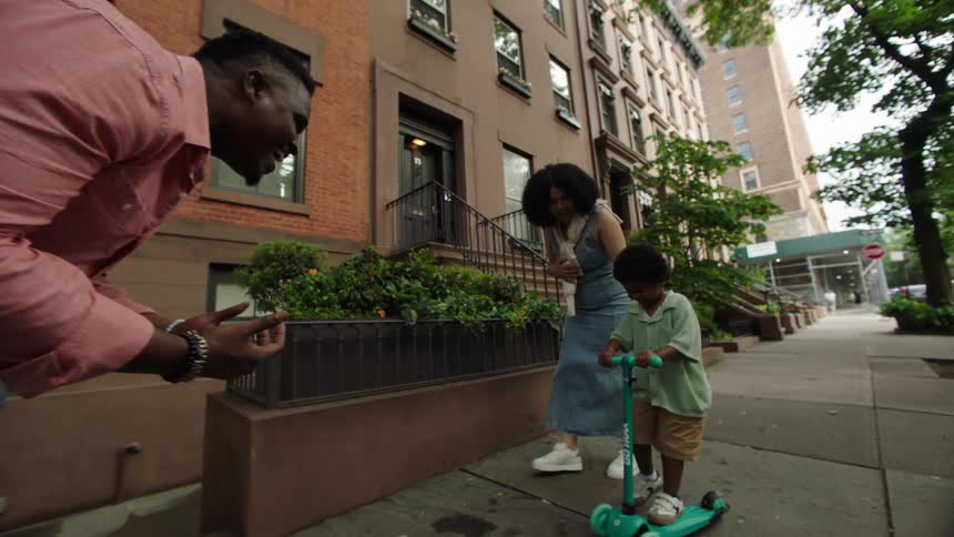 Parents watch their son ride a scooter