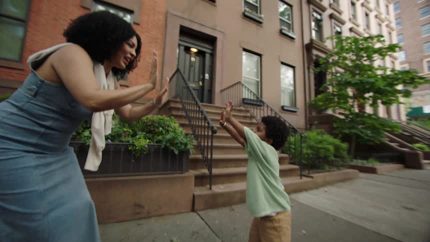 Mother and son touching palms while standing on a suburban sidewalk