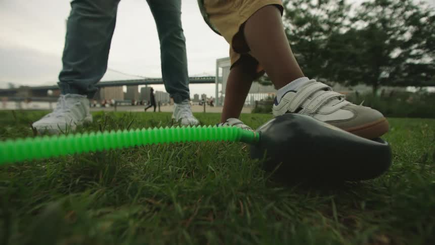 A child steps on a foot pump outdoors with an adult standing nearby