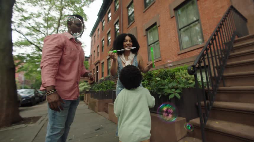 A family enjoys a playful moment blowing bubbles together on a treelined city sidewalk
