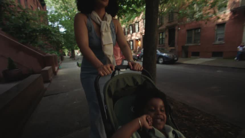 A woman pushing her child in a stroller on the sidewalk with her husband walking behind her at midday