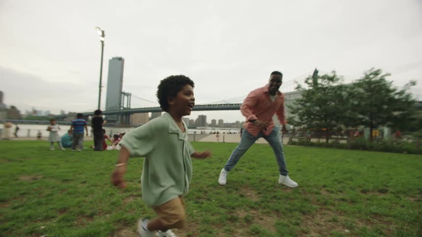 Father plays with his son while they visit a busy riverside park located across from downtown