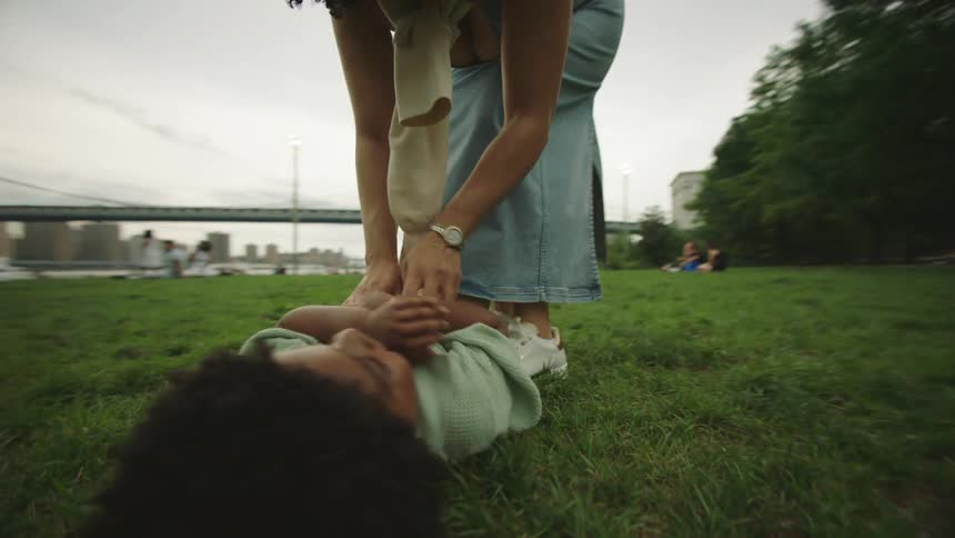Mother tickles son lying on grass in a park