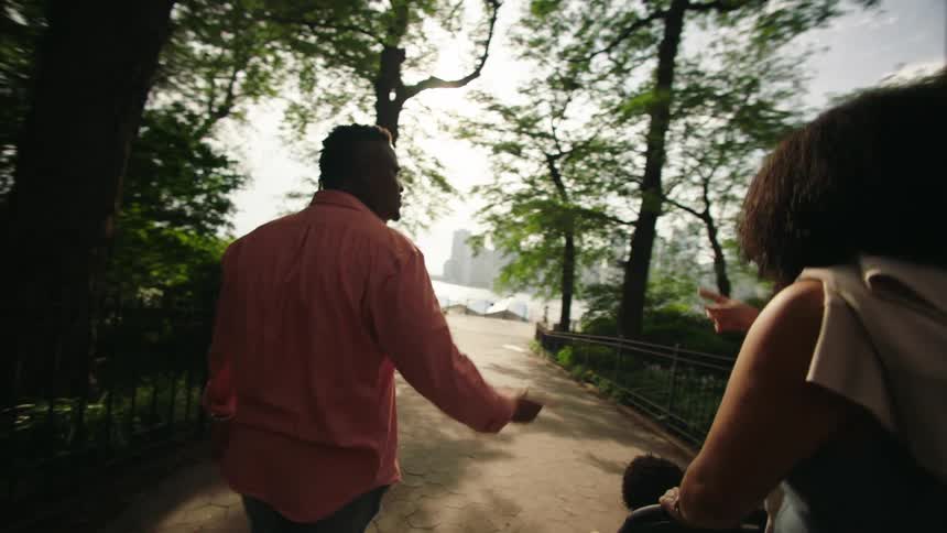 A young couple converse while walking down a path outdoors with their baby in a stroller during daytime