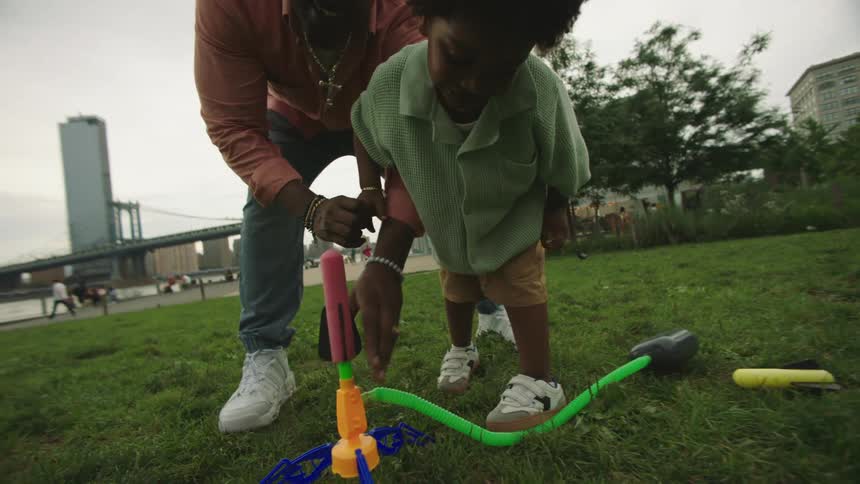 The father and son work together to load a foam rocket launcher in the park