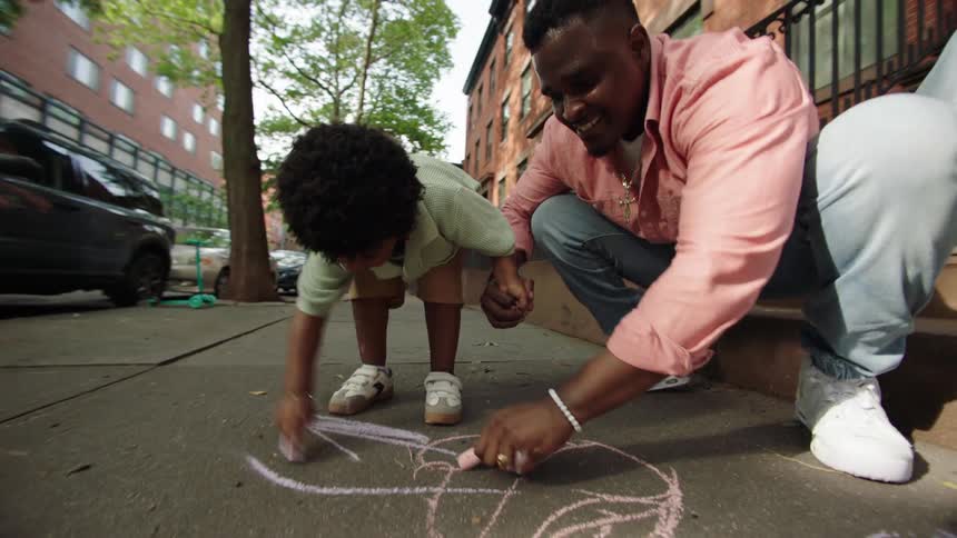 Father and son are drawing with chalk on the sidewalk