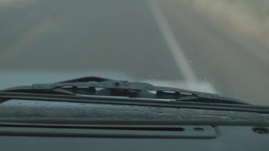Windshield wiper viewed from a vehicle interior while traveling on a two lane highway at dusk during light rain