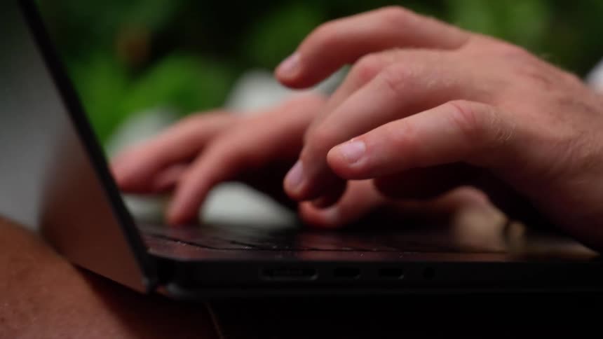 A man typing on his laptop while sitting in an outdoor area at midday