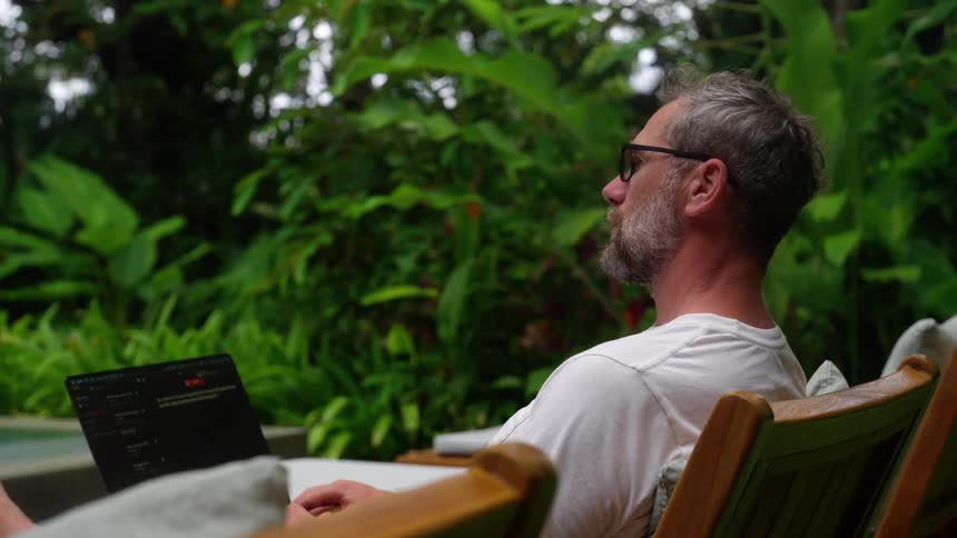 Male working from his laptop while sitting on a lounge chair at a resort