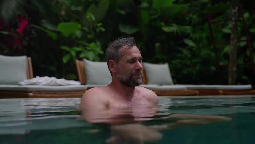 A man relaxes in a swimming pool surrounded by lush greenery