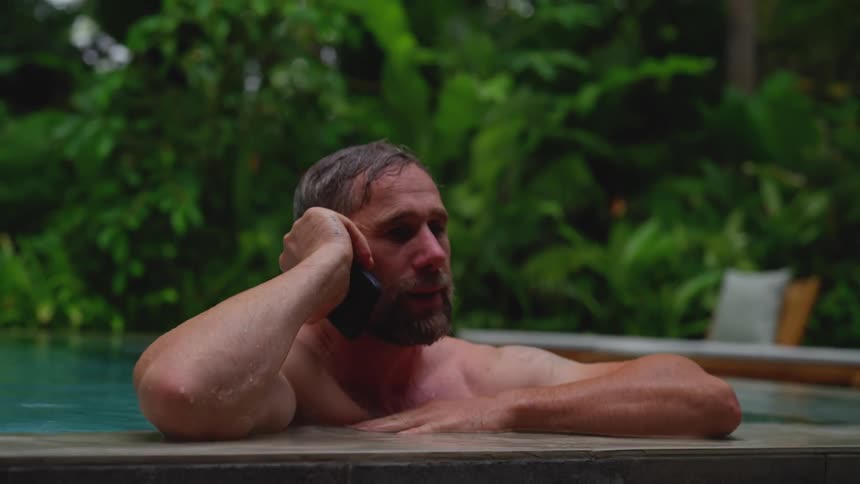 The man answers his phone in the pool