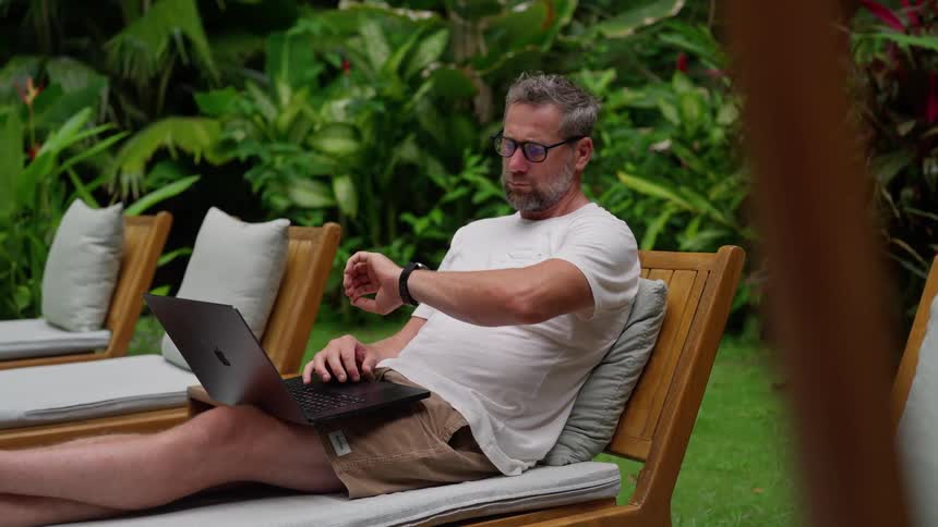 Man works on laptop while lounging outdoors in tropical setting