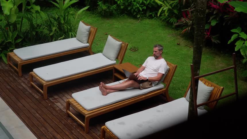 Man relaxing in a chair and typing on a laptop