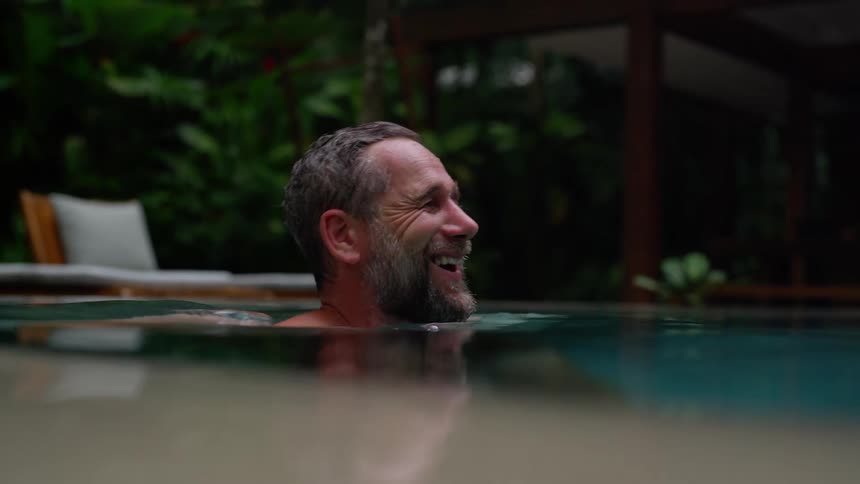 A middleaged man swimming in an outdoor resort pool having fun with a smile on his face