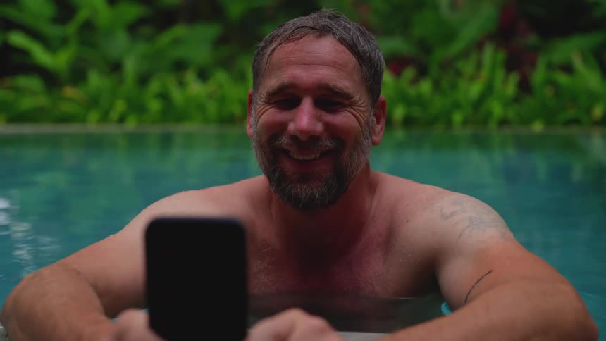 Smiling man holding a smartphone while standing in a swimming pool