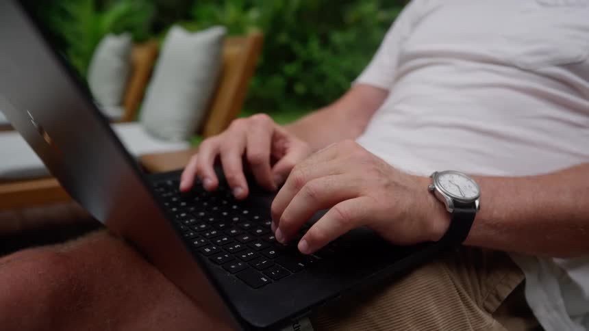 Pair of hands of a person sitting outdoors and typing on a laptop
